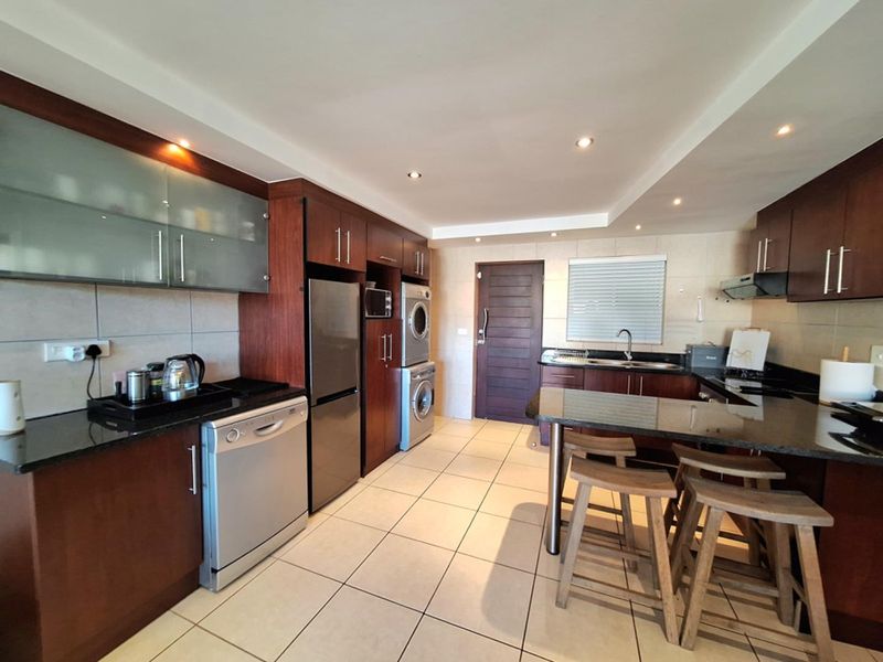 Modern kitchen featuring dark wood cabinetry, granite countertops, integrated appliances, and a breakfast bar with tiled flooring and recessed lighting.
