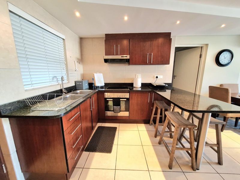 A well-maintained kitchen featuring dark wood cabinetry, granite countertops, a breakfast bar, and integrated appliances including an oven and hob.