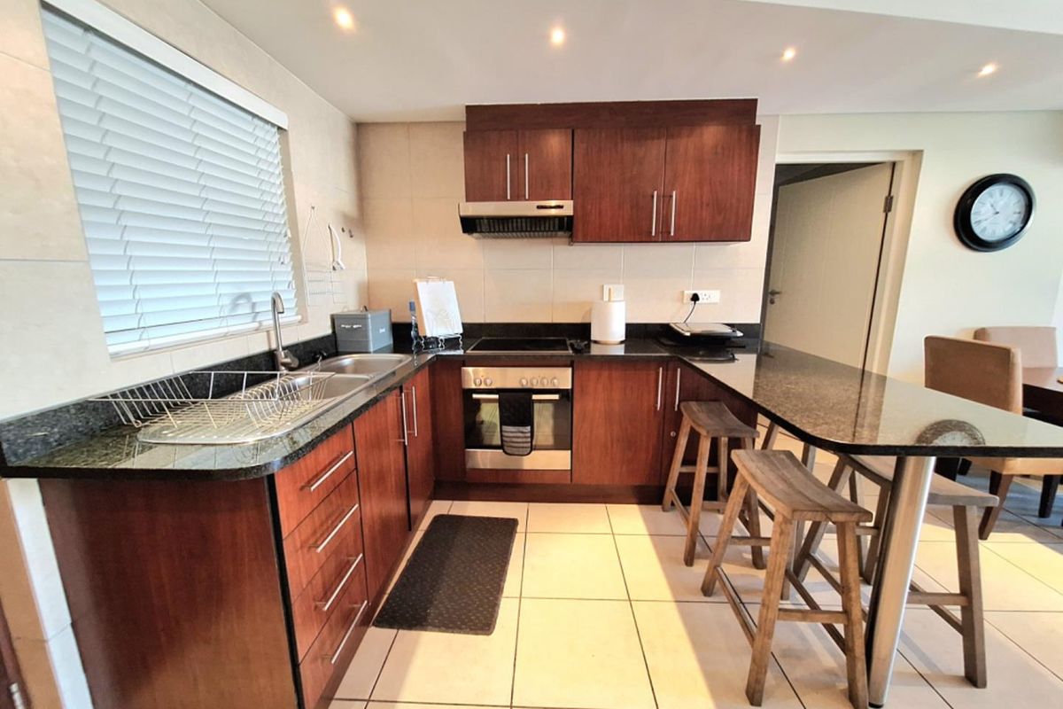 A well-maintained kitchen featuring dark wood cabinetry, granite countertops, a breakfast bar, and integrated appliances including an oven and hob.