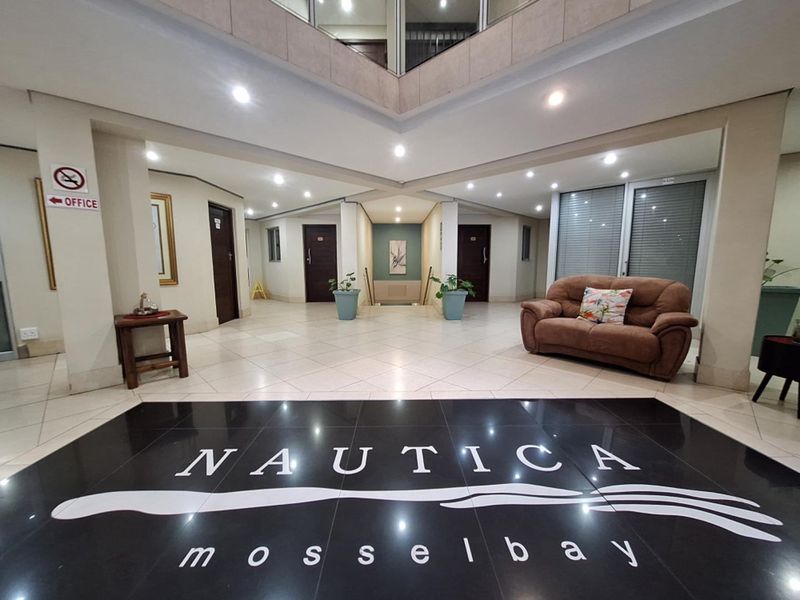 A spacious and well-lit apartment building entrance lobby featuring tiled flooring, recessed lighting, and a central atrium design.