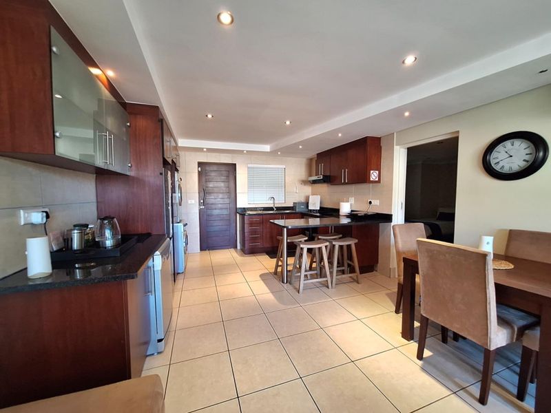 Spacious open-plan kitchen and dining area featuring dark wood cabinetry, granite countertops, tiled flooring, and recessed lighting, creating a functional and cohesive living space.