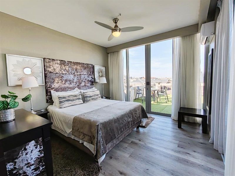 Spacious bedroom featuring wood-look flooring, a ceiling fan, and large sliding glass doors opening onto a private balcony with outdoor views.