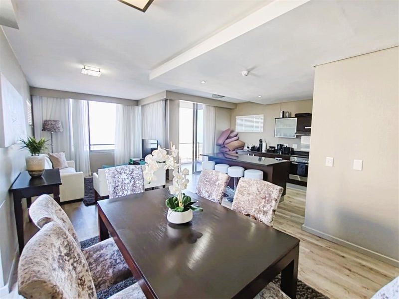Open-plan living and dining area featuring a modern kitchen with a breakfast bar, sleek cabinetry, and integrated appliances, flowing into a bright lounge space.