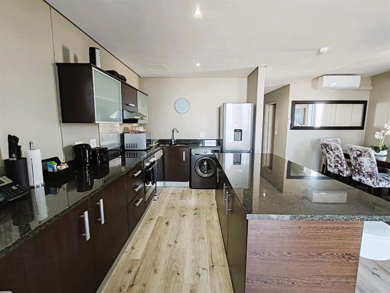 Modern open-plan kitchen featuring dark cabinetry, granite countertops, integrated appliances, and wood-look flooring, seamlessly flowing into the adjacent dining area.