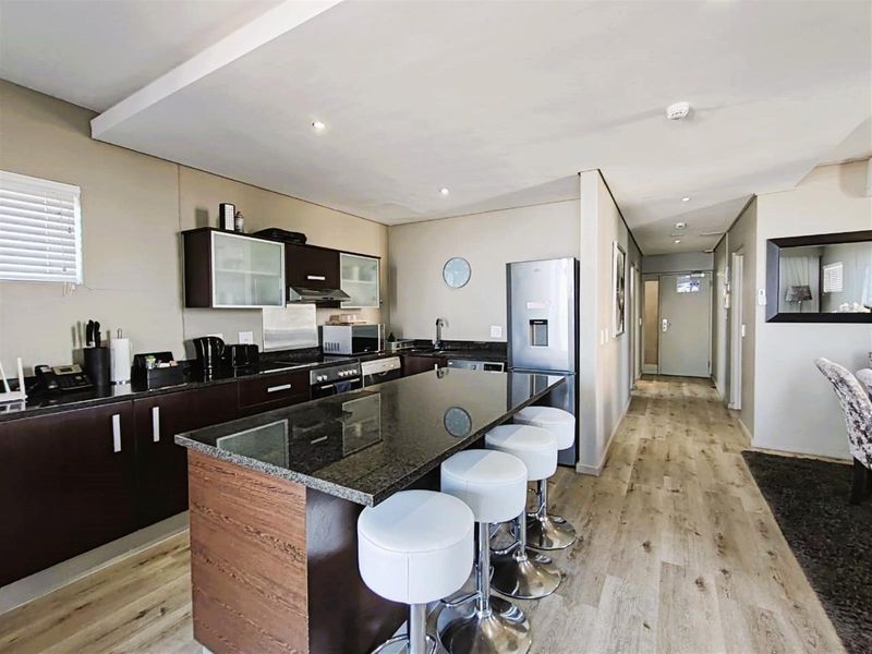 Modern open-plan kitchen featuring dark cabinetry, granite countertops, a central island with breakfast bar seating, and integrated appliances, flowing into the hallway.