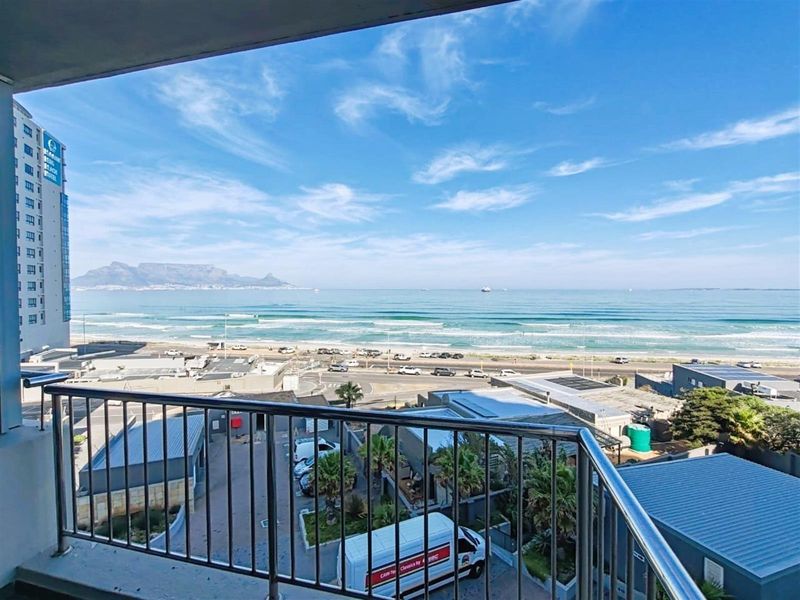 A balcony view overlooking the coastline, beach, and distant mountain range, featuring a metal safety railing.