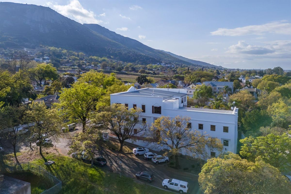 Aerial view of a multi-story office building featuring a white facade, set within a landscaped environment with mountain views.