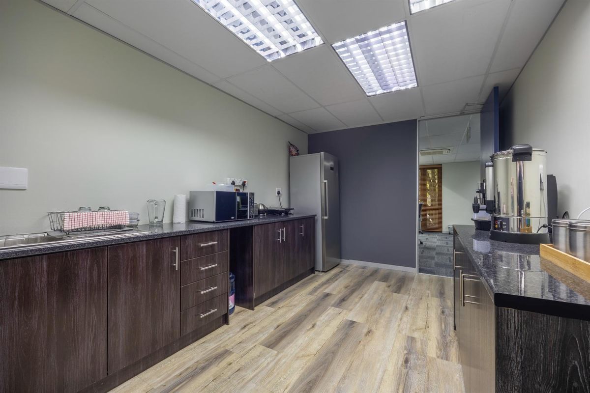 A functional office kitchenette featuring dark wood cabinetry, granite-style countertops, recessed ceiling lighting, and durable wood-look vinyl flooring.
