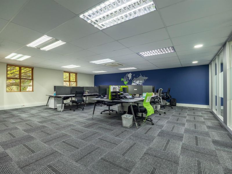 A modern, open-plan office space featuring carpeted flooring, recessed grid lighting, and a glass-partitioned wall, providing a professional and functional work environment.