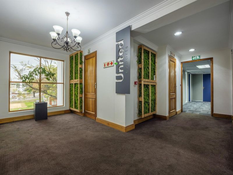 A professional office lobby featuring carpeted flooring, decorative wall-mounted greenery, wooden door frames, and a chandelier, providing a welcoming entrance area.