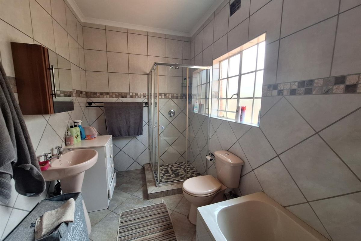 A functional bathroom featuring a separate shower enclosure, bathtub, pedestal sink, and toilet with neutral wall and floor tiling.
