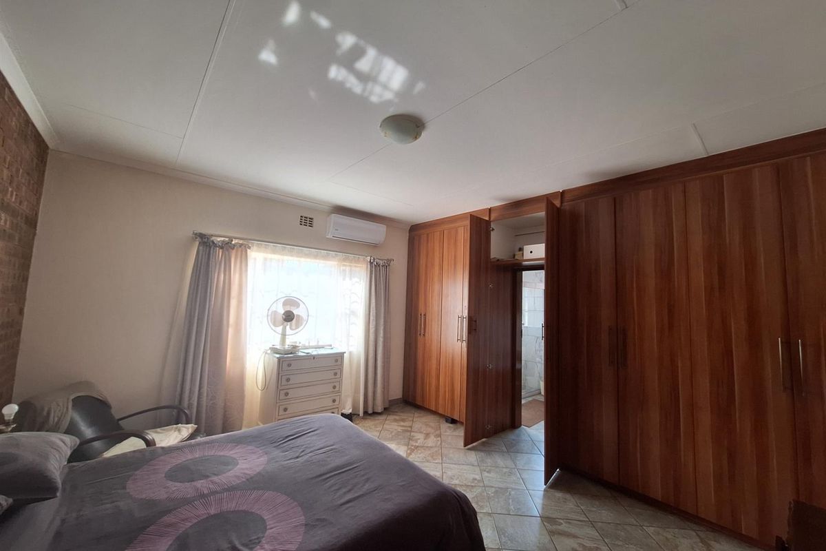 A bedroom featuring built-in wooden cabinetry, tiled flooring, and a wall-mounted air conditioning unit.