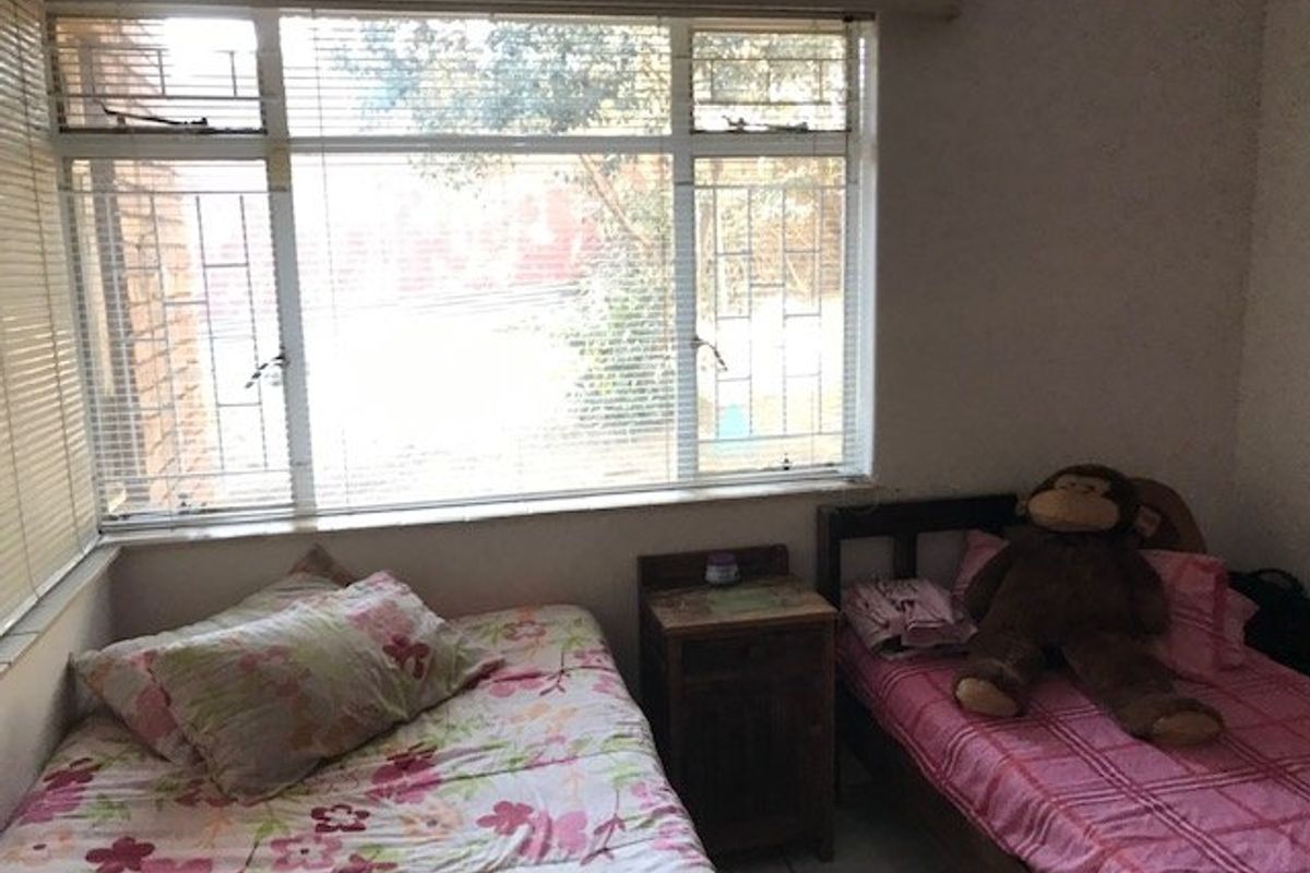 A bedroom featuring large windows with security bars, tiled flooring, and space for two single beds.