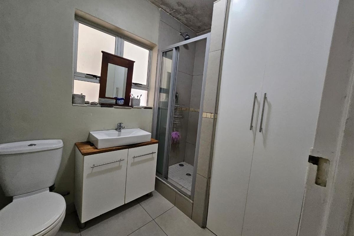 A functional bathroom featuring a shower enclosure, vanity basin, and toilet, with visible signs of wear on the ceiling and finishes.