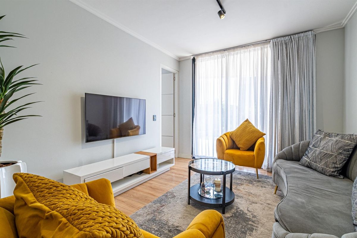 A bright and modern living room featuring laminate flooring, track lighting, and large windows with floor-to-ceiling curtains.