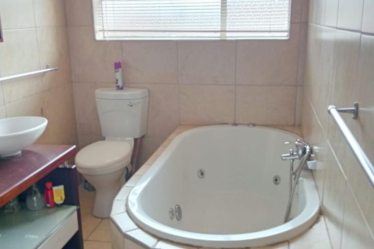 A functional bathroom featuring a built-in corner spa bathtub, a ceramic toilet, and a vanity basin with tiled walls and flooring.