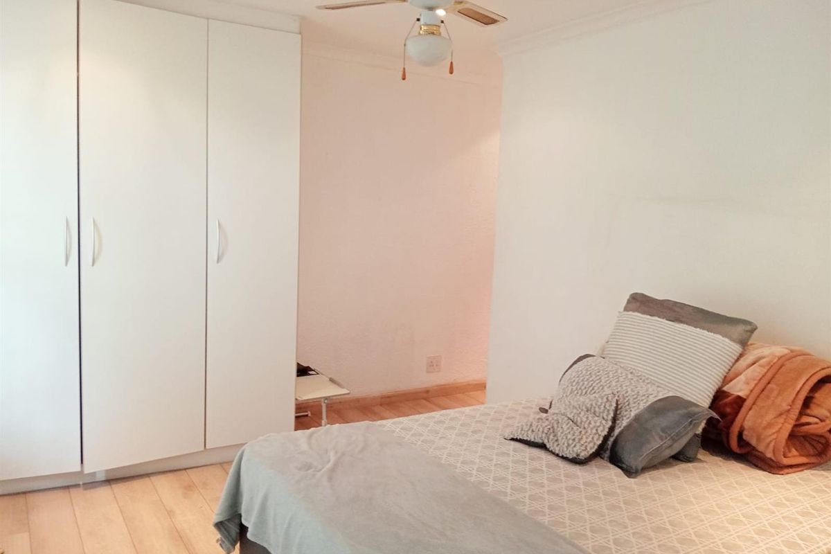 A bedroom featuring built-in wardrobes, light wood-look flooring, and a ceiling fan.