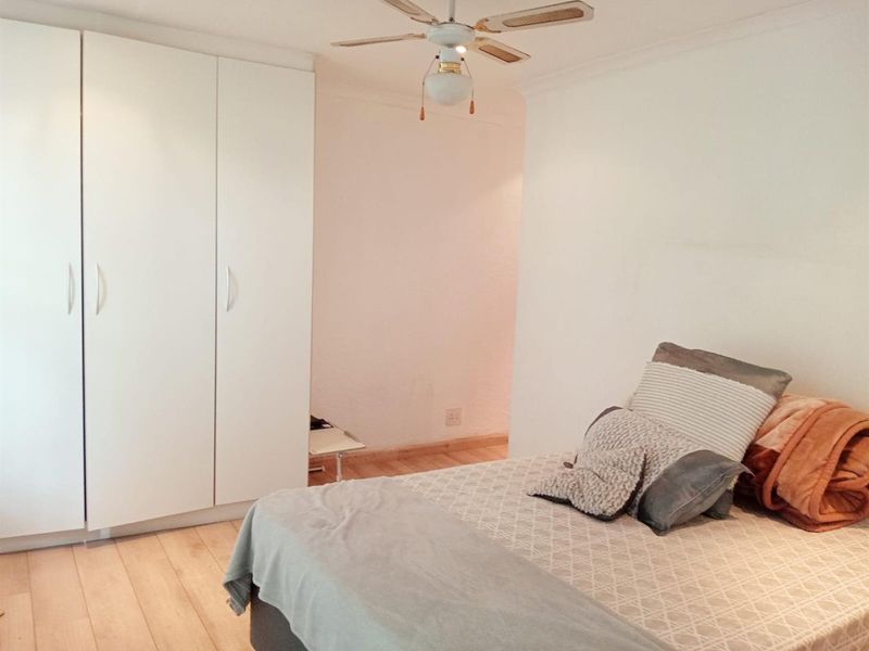 A bedroom featuring built-in wardrobes, light wood-look flooring, and a ceiling fan.