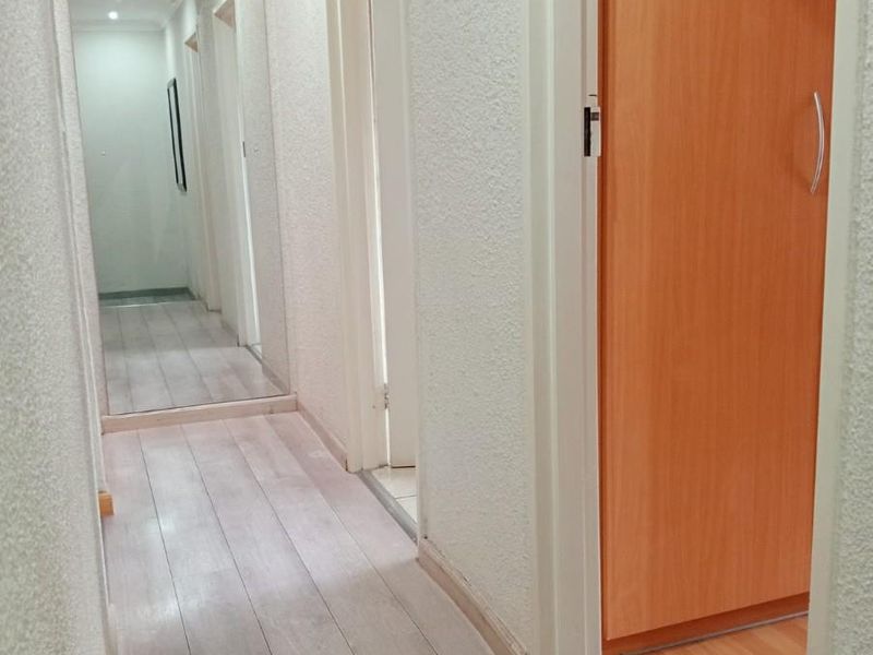 A bright hallway featuring light-toned laminate flooring, textured wall finishes, and multiple interior doors leading to adjacent rooms.