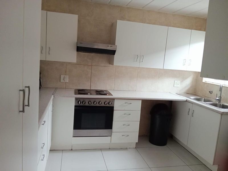 A functional kitchen featuring white cabinetry, tiled splashbacks, a built-in oven with hob, extractor fan, and a double-basin sink.