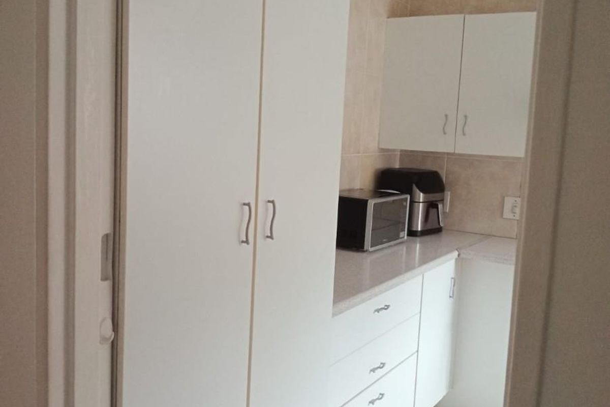A compact kitchen featuring white cabinetry, laminate countertops, tiled backsplash, and tiled flooring, providing a clean and functional workspace.