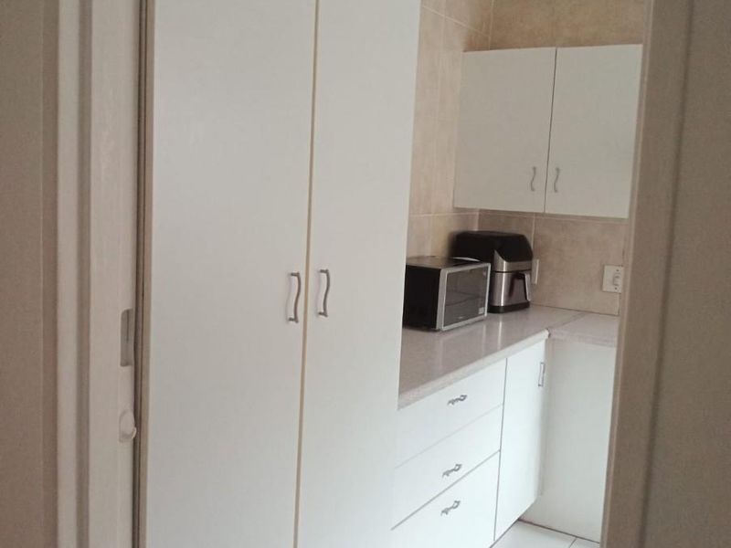 A compact kitchen featuring white cabinetry, laminate countertops, tiled backsplash, and tiled flooring, providing a clean and functional workspace.