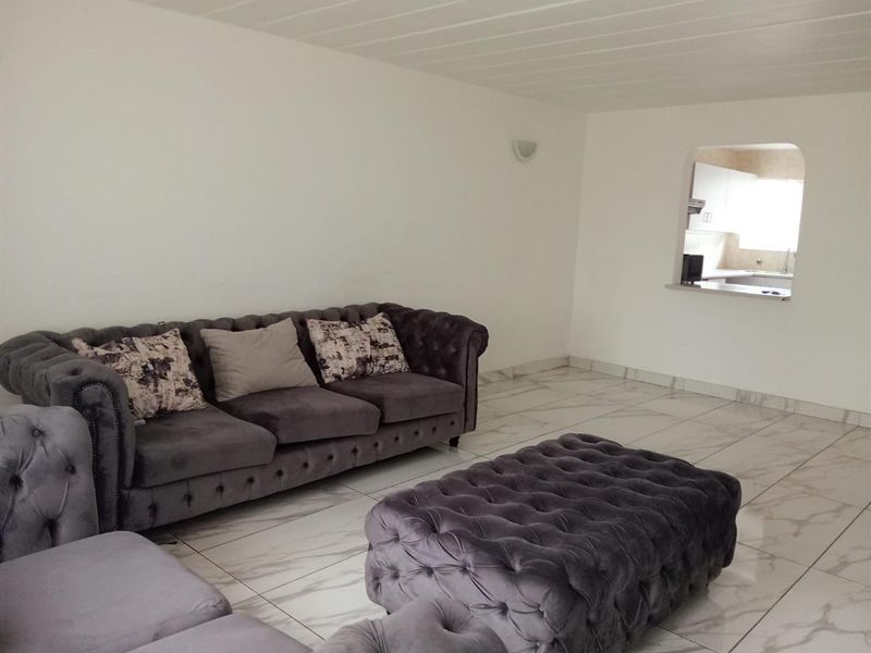 Open plan living area featuring marble-look floor tiles and a service window connecting to the kitchen.