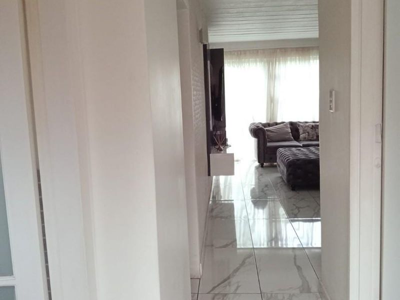 A bright hallway featuring polished marble-look floor tiles, leading into an open-plan living area with natural light.