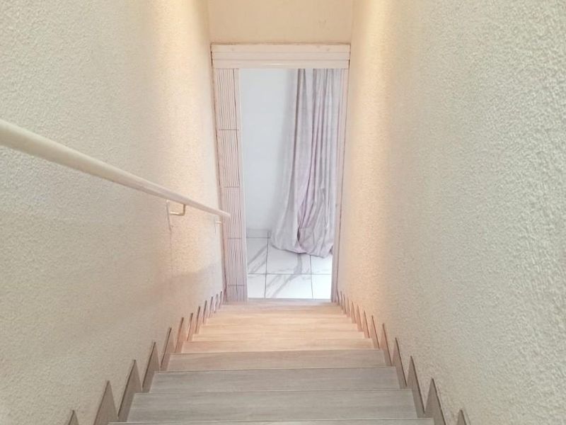 A staircase with light wood-look treads and a simple handrail, leading down to a tiled landing area.