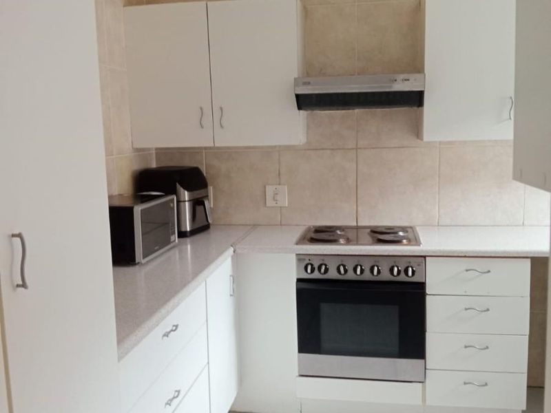 A compact kitchen featuring white cabinetry, tiled splashbacks, tiled flooring, and a built-in oven with an extractor fan.
