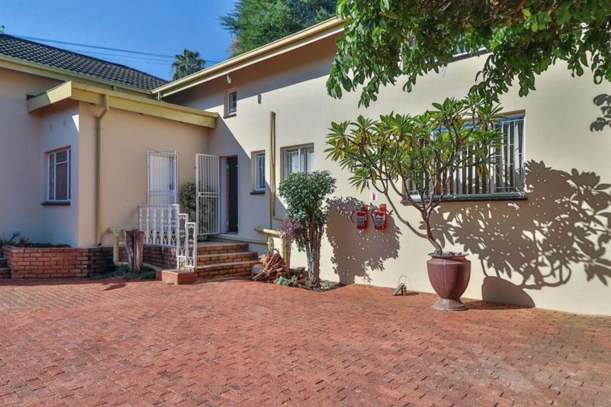 Rear exterior view of the property featuring a brick paved courtyard, security gates, and wall-mounted fire safety equipment.