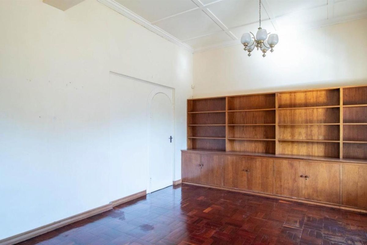 A spacious living area featuring classic parquet flooring, a large built-in wooden bookshelf, and an elegant arched doorway.