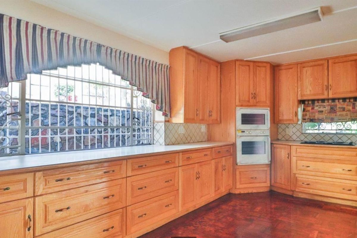 A traditional kitchen featuring extensive wooden cabinetry, a built-in double oven, integrated hob, and tiled backsplash with security bars on the window.