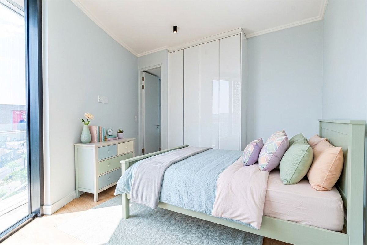 A bright and modern bedroom featuring light-toned timber flooring, a sleek built-in wardrobe, and a large sliding glass door providing ample natural light.