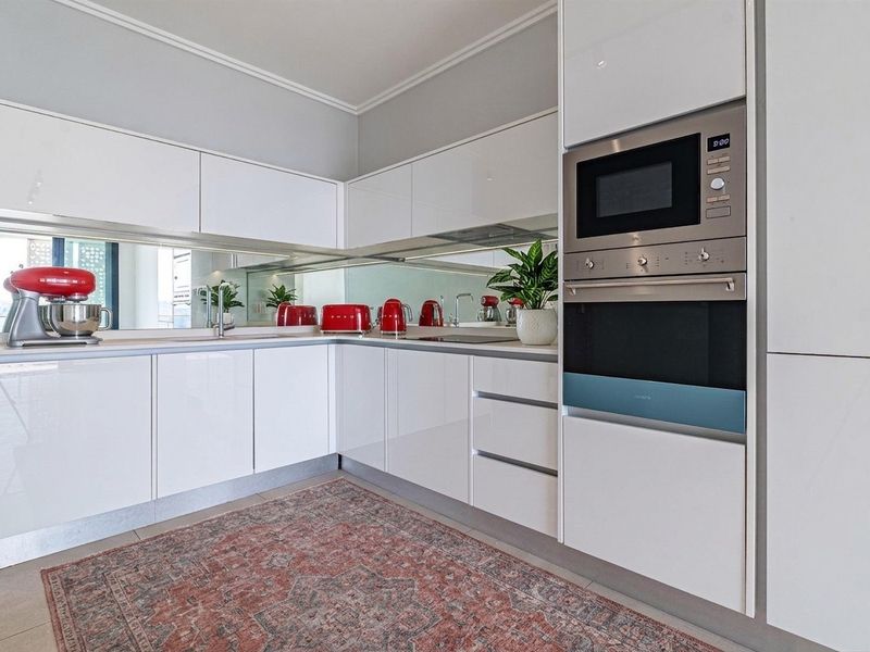 Modern kitchen featuring high-gloss white cabinetry, a mirrored splashback, and integrated stainless steel appliances including a built-in oven and microwave.
