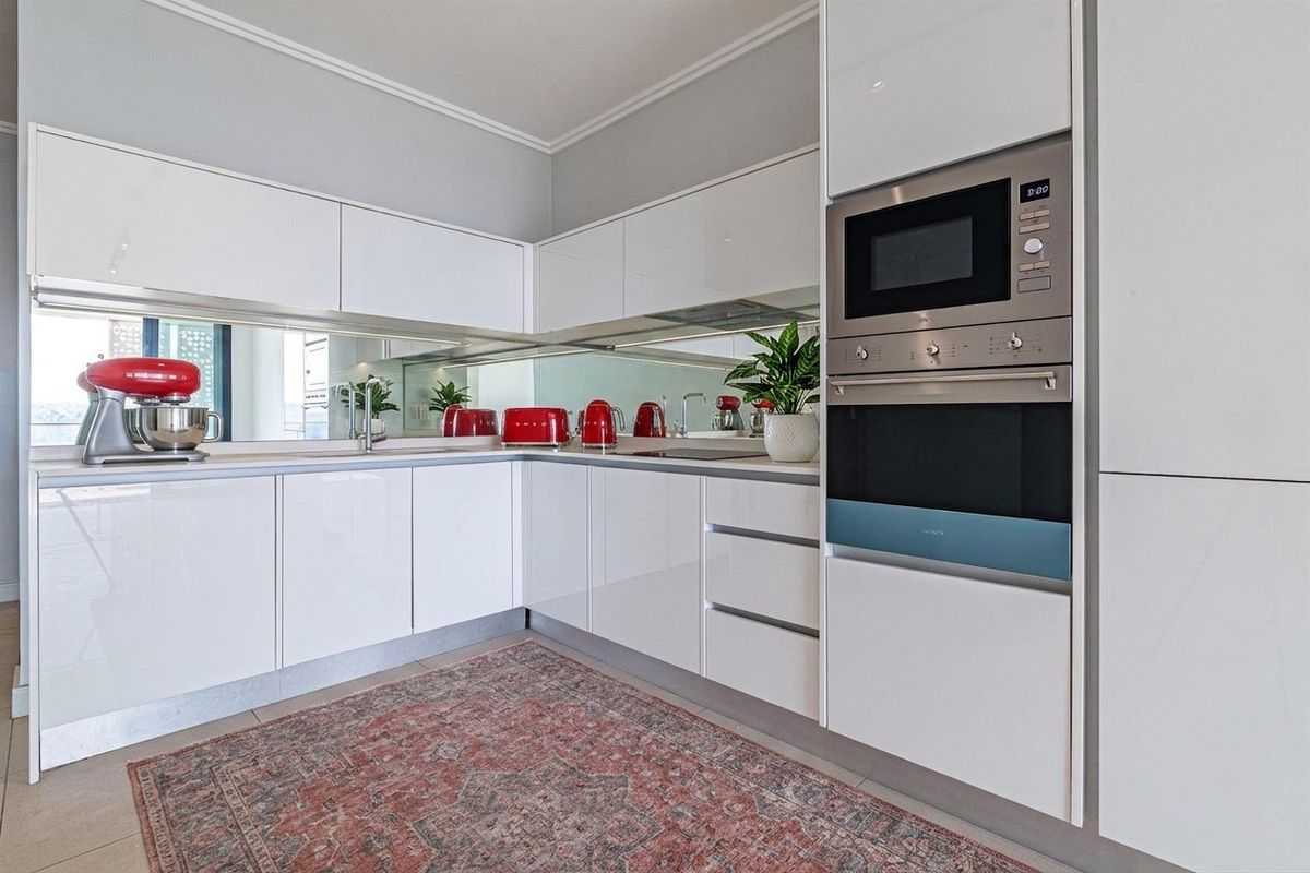 Modern kitchen featuring high-gloss white cabinetry, a mirrored splashback, and integrated stainless steel appliances including a built-in oven and microwave.