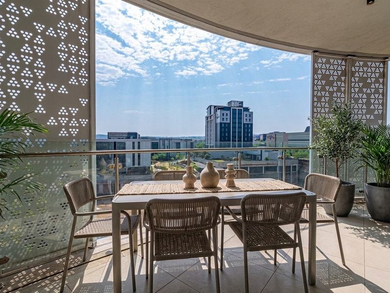 A spacious covered balcony featuring decorative metal privacy screens, a glass balustrade, and tiled flooring, offering expansive urban views.