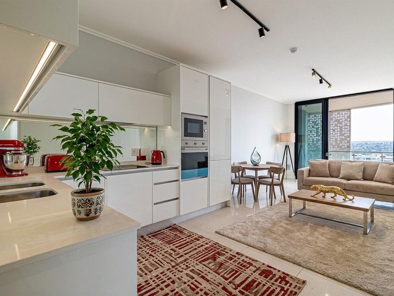 Modern open-plan apartment featuring a sleek kitchen with integrated appliances, stone countertops, and seamless flow to a balcony with expansive views.