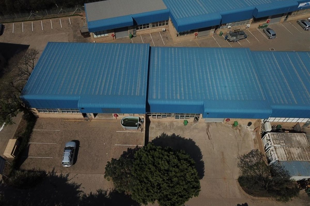Aerial view of an industrial complex featuring multiple warehouse units with blue corrugated metal roofing and dedicated parking bays.