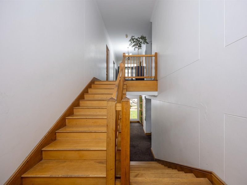 A central wooden staircase with a landing, connecting different levels of the office building with a functional and traditional design.