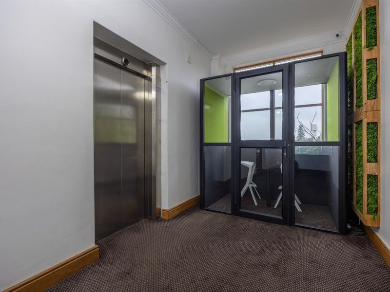 Office lobby area featuring a stainless steel elevator, a glass-enclosed meeting pod, and a vertical garden wall feature.
