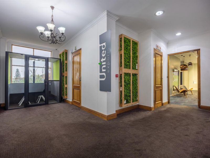 A professional office hallway featuring wooden doors, integrated vertical garden panels, recessed lighting, and a decorative chandelier.