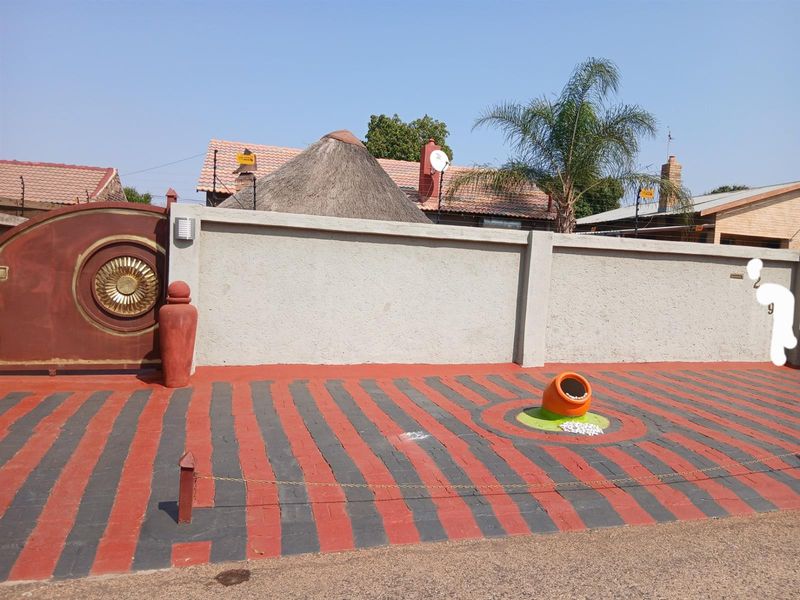 Front exterior view featuring a paved driveway, boundary wall with electric fencing, and a decorative entrance gate.