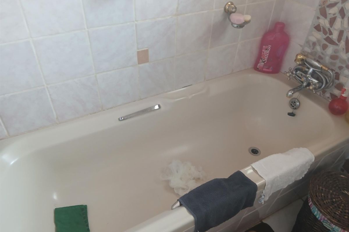A dated bathroom featuring a standard bathtub with wall tiling and chrome fixtures, requiring cosmetic updates to modernize the space.