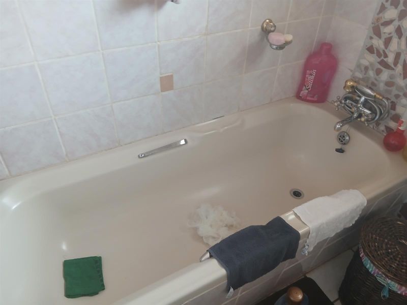 A dated bathroom featuring a standard bathtub with wall tiling and chrome fixtures, requiring cosmetic updates to modernize the space.