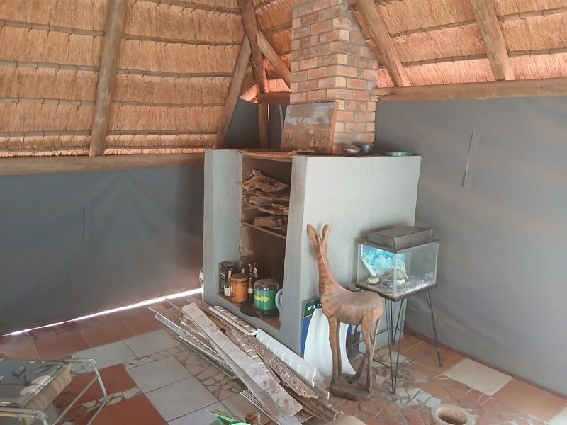 Covered outdoor patio area featuring a traditional thatched roof, exposed timber rafters, and a built-in brick fireplace with tiled flooring.