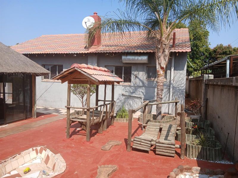 Rear exterior view of the property featuring a tiled roof, solar geyser, chimney, and a paved outdoor area with established garden elements.