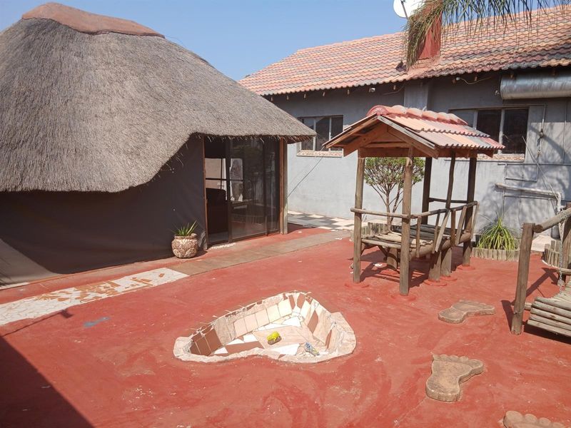 Rear exterior area featuring a thatched roof structure, paved patio, and a built-in fire pit, providing a rustic outdoor entertainment space.