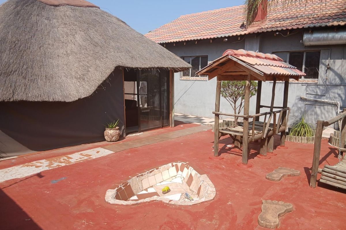 Rear exterior area featuring a thatched roof structure, paved patio, and a built-in fire pit, providing a rustic outdoor entertainment space.