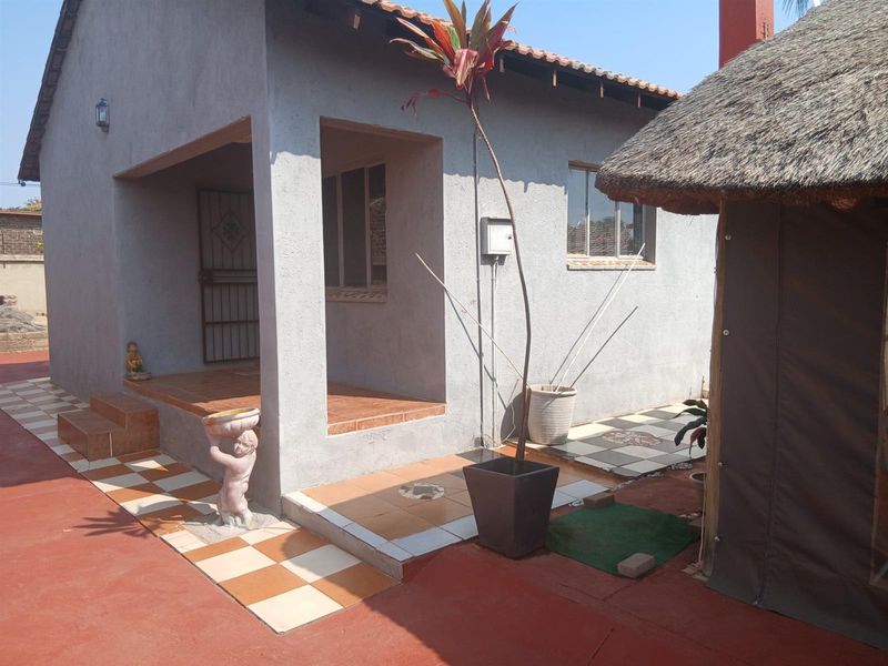 Rear view of the property featuring a covered patio area, tiled walkways, and an adjacent thatched structure in a residential setting.